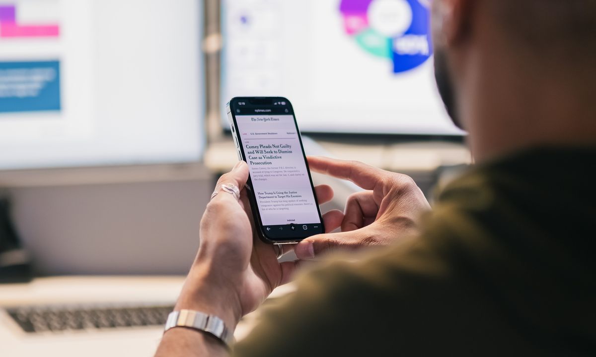 A professional using a smartphone alongside business systems in an office.